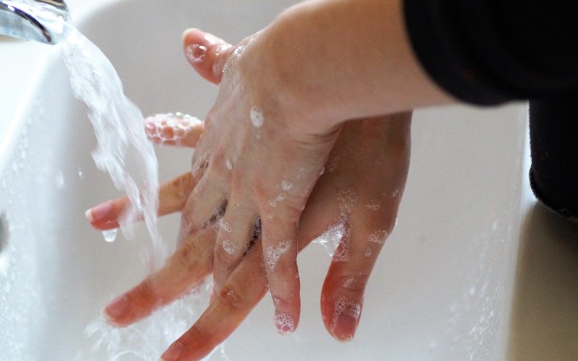 Uma pessoa esfregando as mãos com sabão, embaixo da torneira.