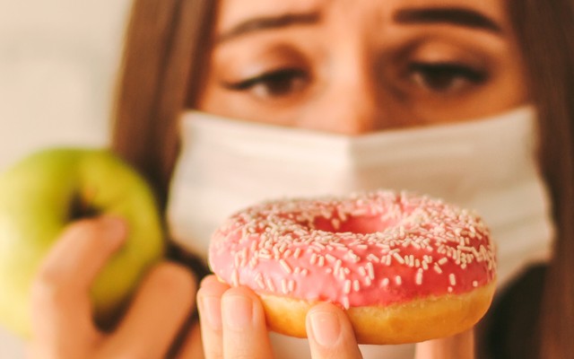 Mulher com mascara olhando de forma triste para um donut.