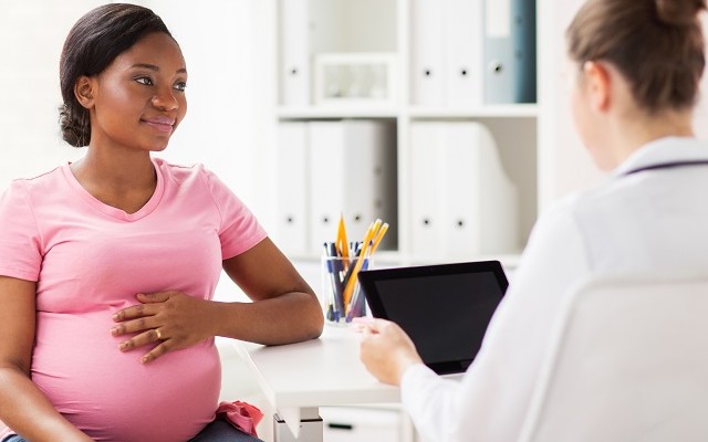 Mulher grávida com camiseta rosa em um consultório recebendo orientações de uma médica durante o pré-natal.