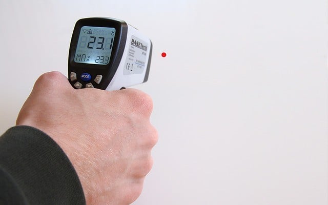 Uma pessoa apontando um termômetro infravermelho para a parede.