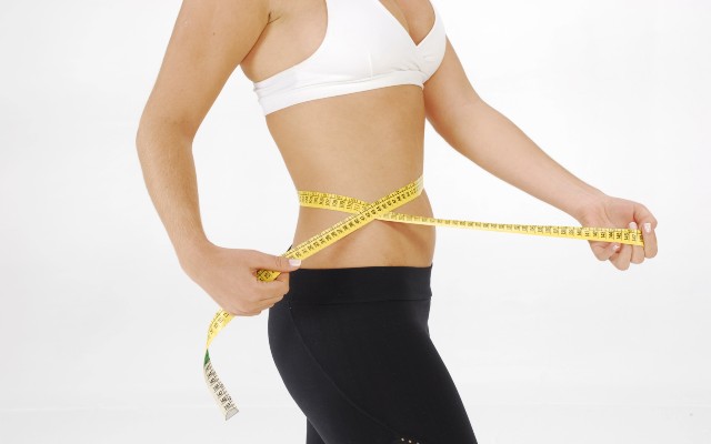 Mulher medindo a cintura com fita métrica.