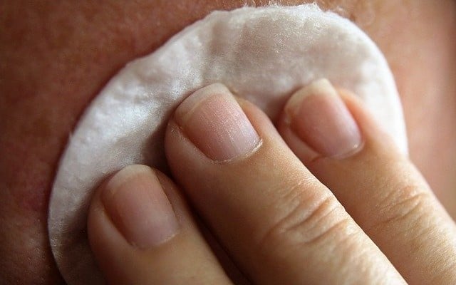 Mulher limpando a espinha interna no rosto com um disco de algodão.
