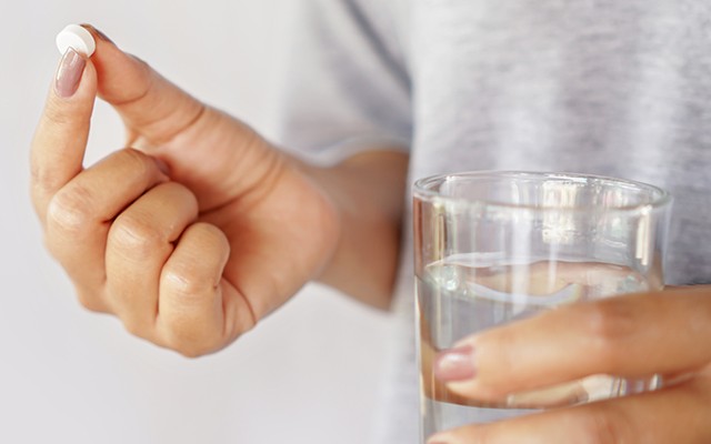 Mulher com um comprimido de metformina de metformina na mão e um copo de água.