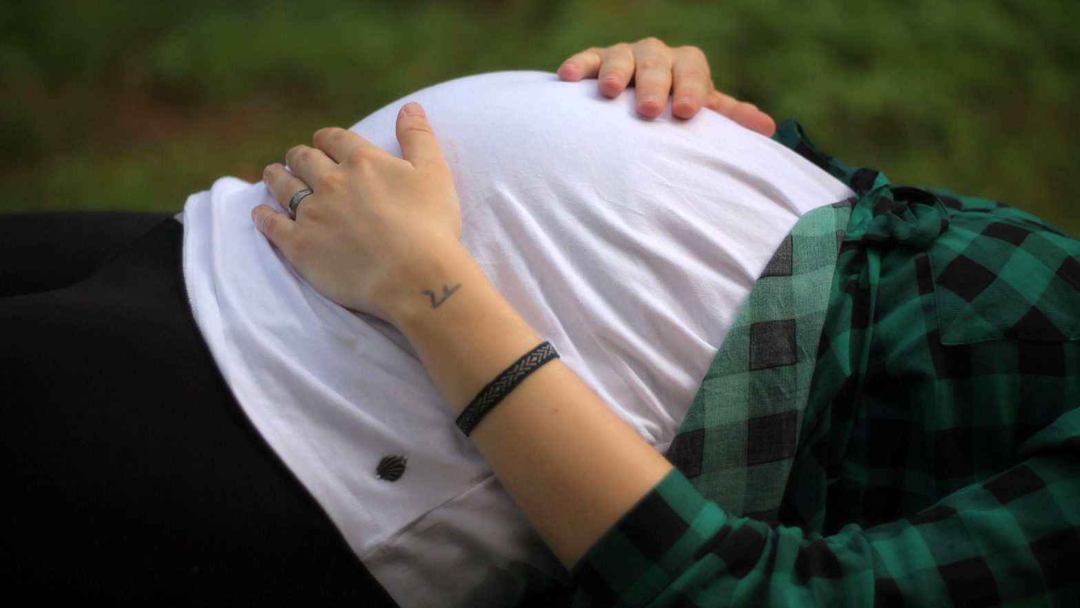 Mulher grávida com as mãos na barriga deitada na grama.