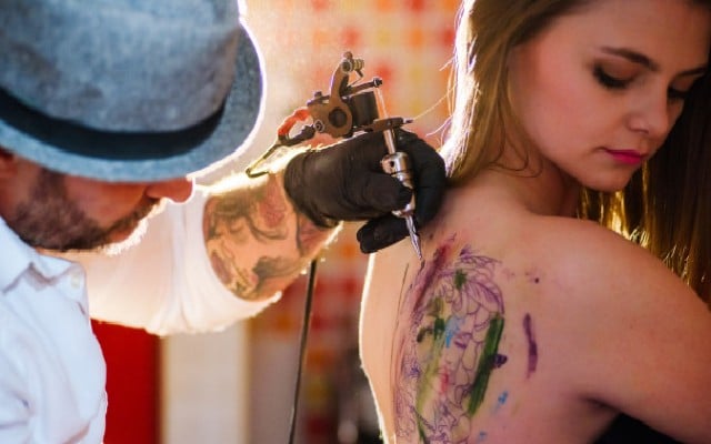 Homem fazendo tatuagem nas costas de uma mulher.