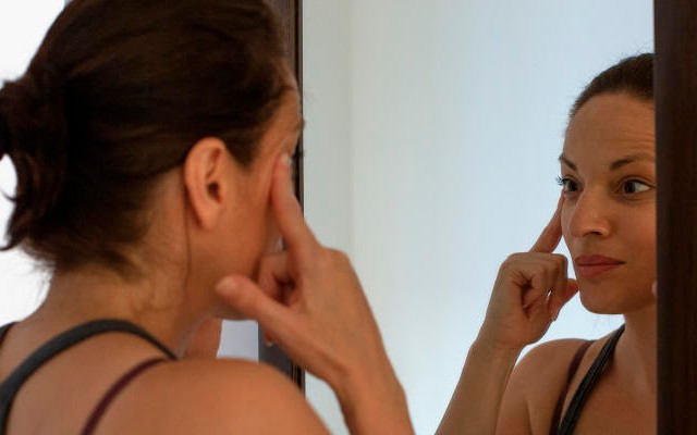 Mulher em frente ao espelho praticando yoga facial.