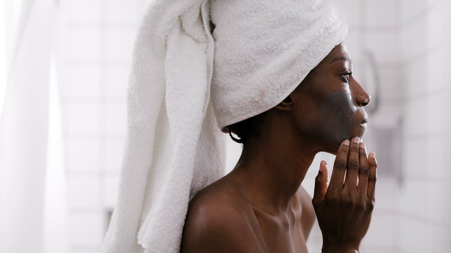 Mulher após sair do banho com toalha na cabeça passando argila no rosto.