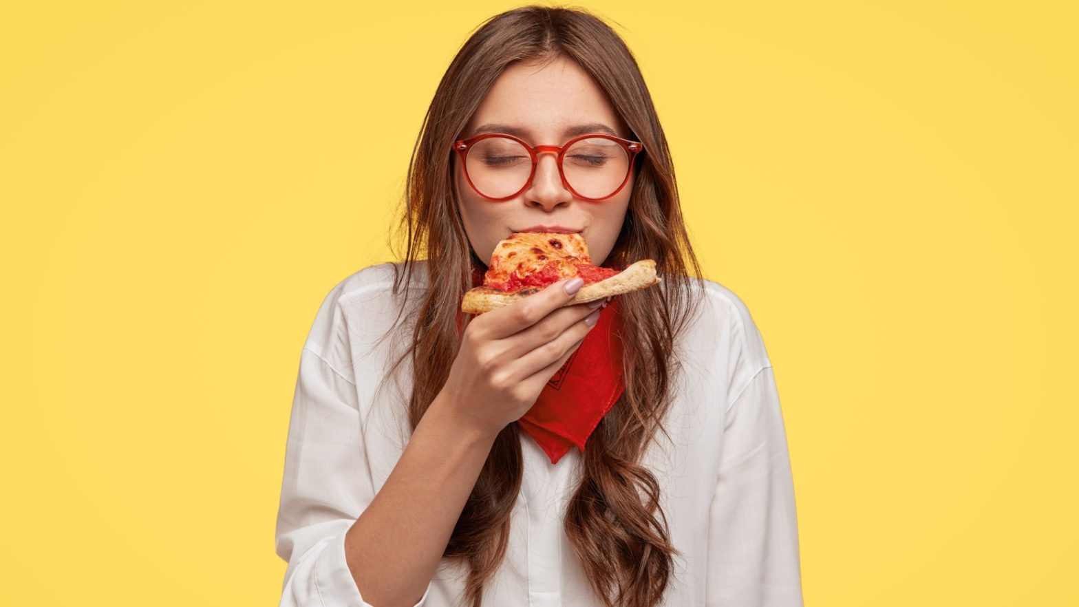 Mulher com expressão facial de prazer enquanto come um pedaço de pizza.